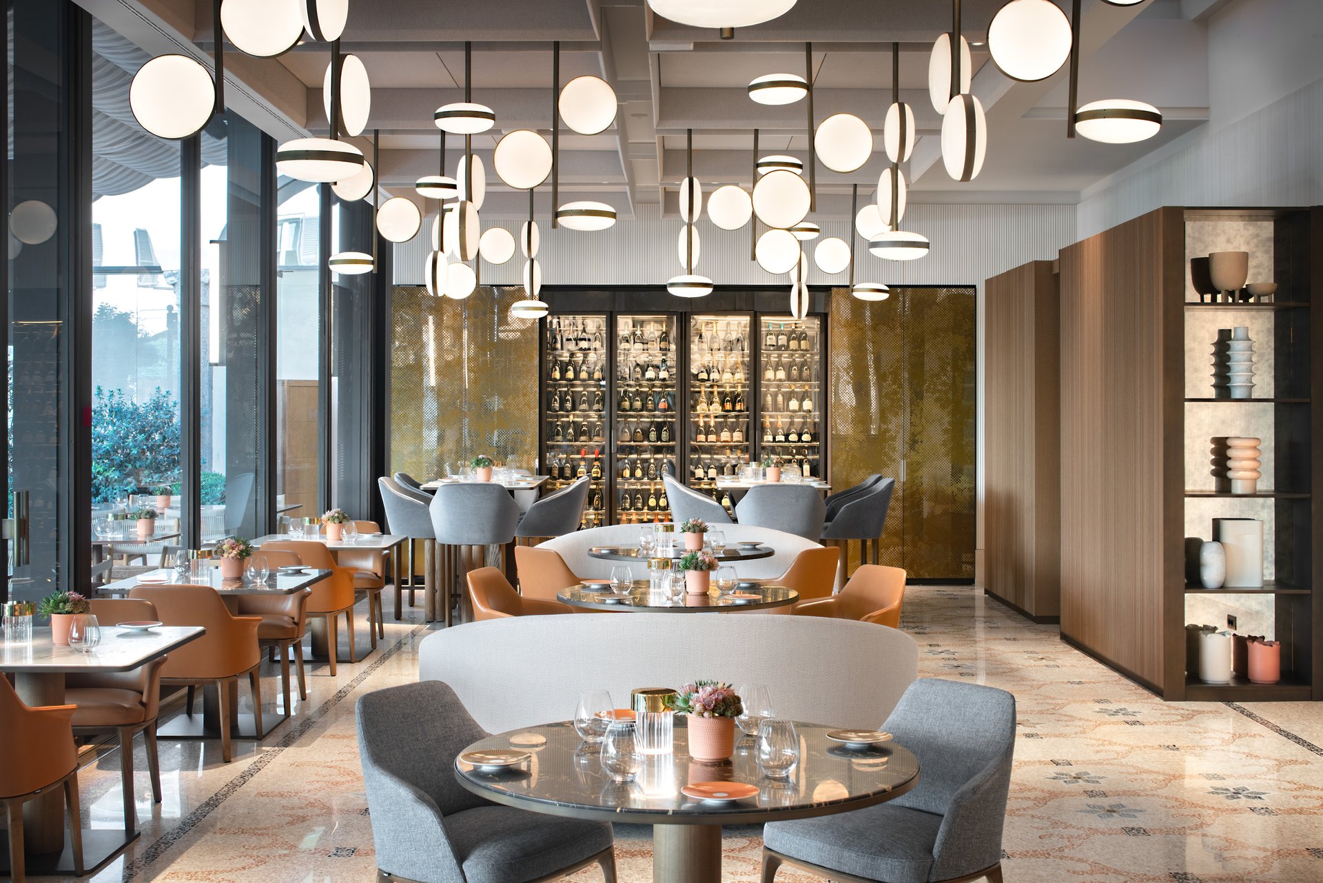 A dining room at the Four Seasons Hotel Milano, under a cloud of globe lights, with a glass-fronted wine wall
