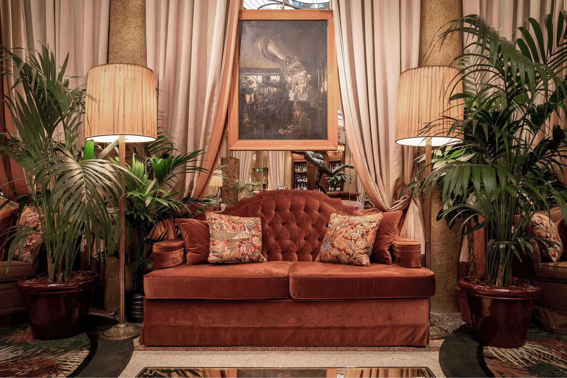 A velvet sofa between palms and silk curtains in the lounge of the Grand Hotel et de Milan