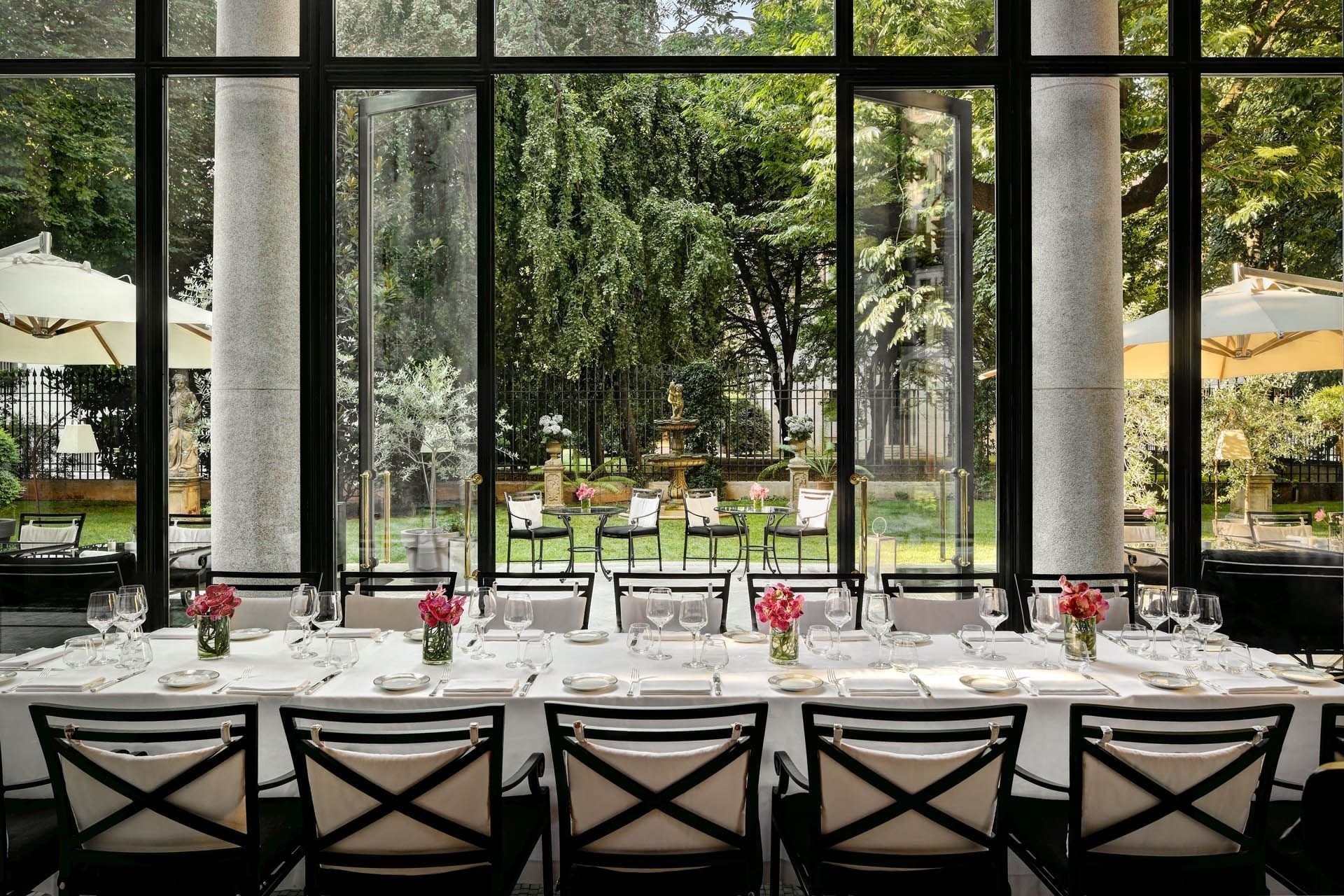 A long table laid in the glass winter garden of Palazzo Parigi, looking onto the hotel's garden