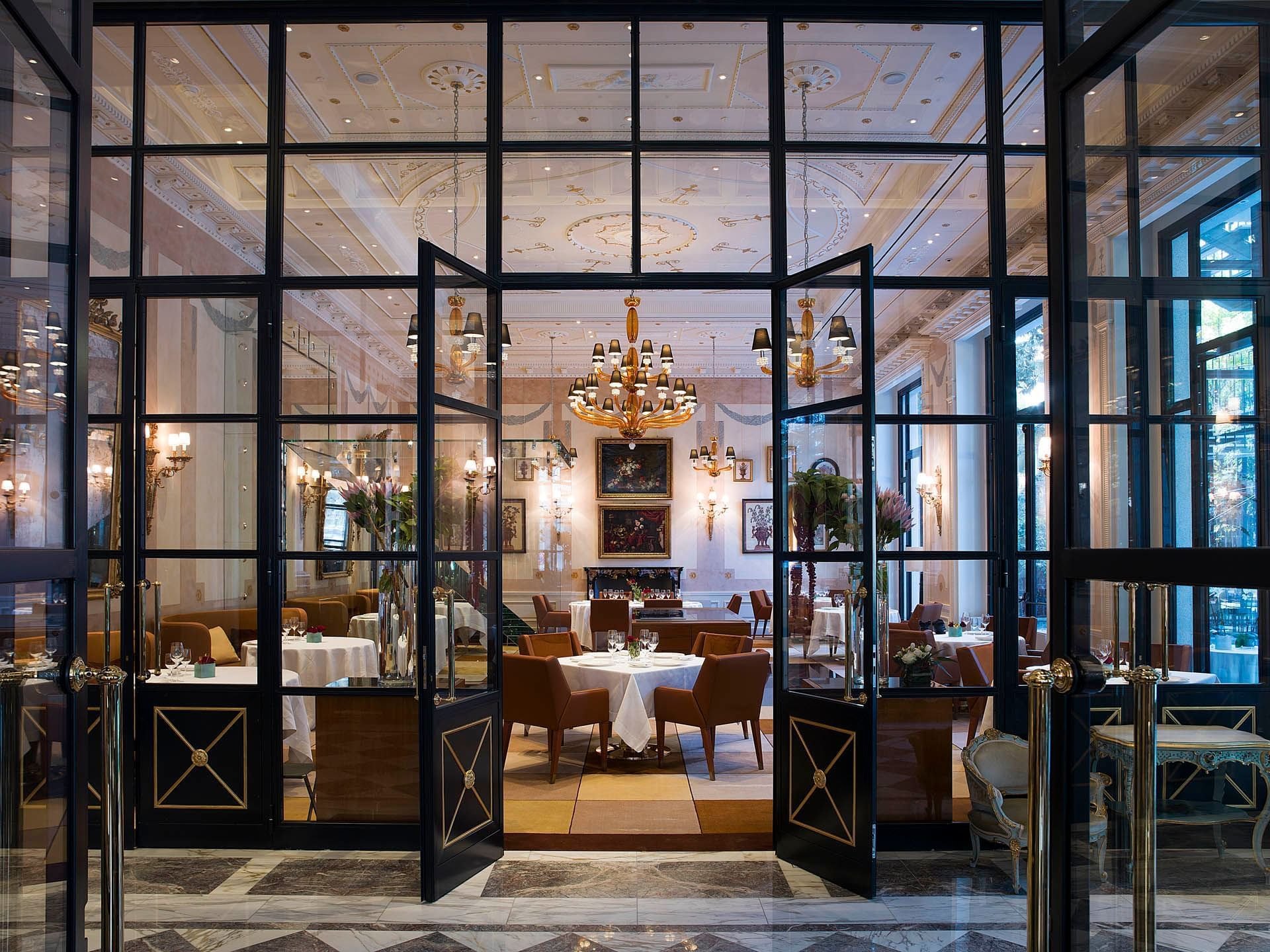 The restaurant of Palazzo Parigi seen through black-framed glass doors, with a chandelier over the tables